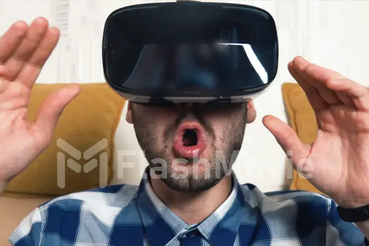 Bearded cheerful young man uses his VR virtual reality glasses at home on the couch