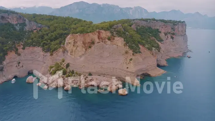 Top view of a rocky shore covered with green trees. Cave in the rock. Blue clear water. Seascape.