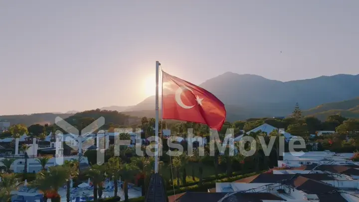 Turkish flag at sunset against the backdrop of the hotel. Swimming pool and palm trees. Mountain