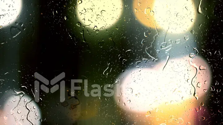 Drops of rain flow down the glass against the bokeh background of moving cars