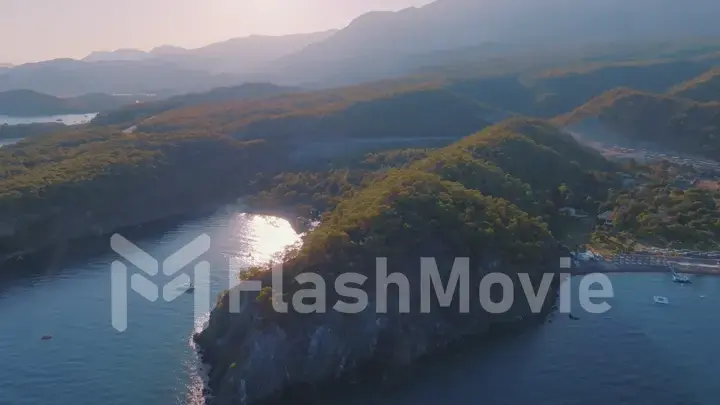 Top view of the bay at sunset. Dense forest on the coast. Water transport floats. Light fog. Aerial drone view