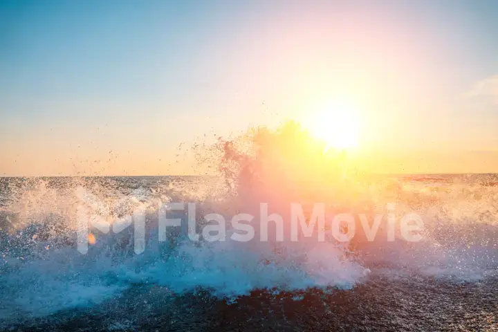 The sun shines through the spray of a sea wave from the shore