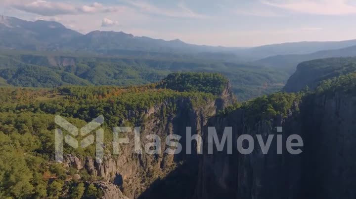 Video footage from a drone flying over a canyon in a mountainous area. Sunny day. Green trees. Natural landscape