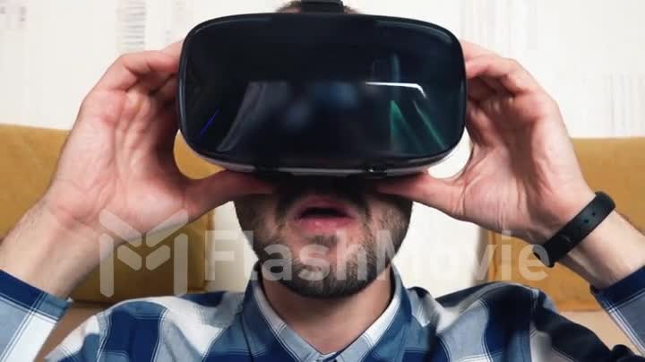 Bearded cheerful young man uses his VR virtual reality glasses at home on the couch