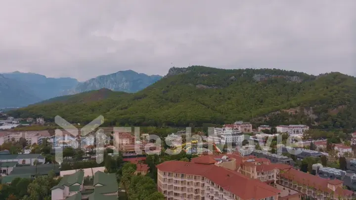 Top view of small resort town. Hotels, houses and roads. Green hills around. Rooftops. Panorama.