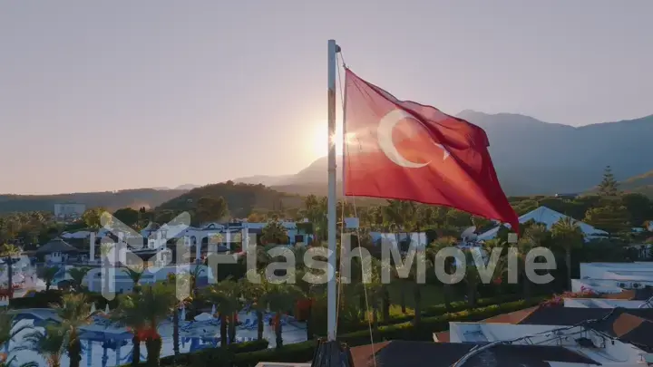 Aerial view of the flag flying on the roof. Sunset. Swimming pool, palm trees and mountains in the background