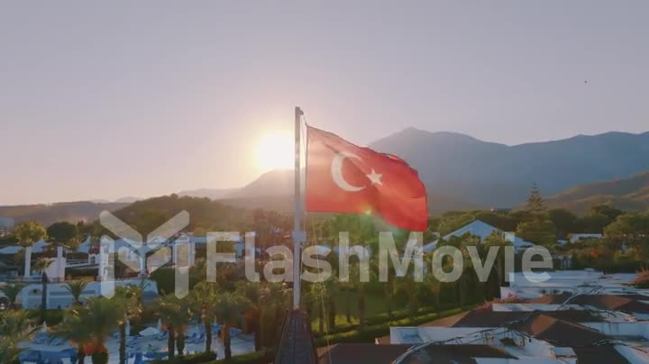 Turkish flag at sunset against the backdrop of the hotel. The hotel grounds, swimming pool and palm trees. Mountain.