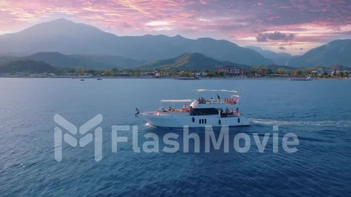 Aerial drone video footage of a seascape. The yacht is sailing fast on the blue sea against the backdrop of sunset.