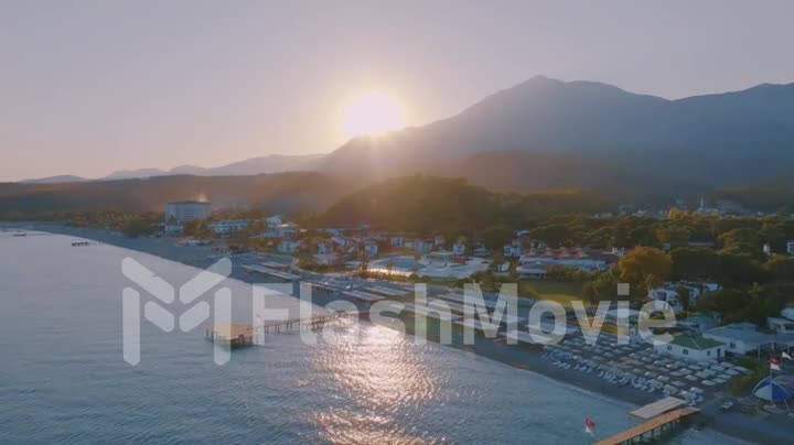 Aerial drone video footage seascape at sunset. Pier. Sandy beach, umbrellas, sun loungers. Mountains in the background