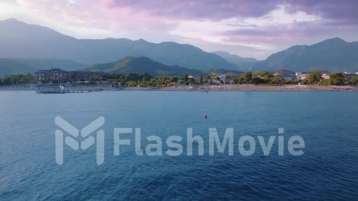 Beautiful sunset. Aerial footage from drone flight over blue sea. Coast and mountains in the background. Seascape. Buoy