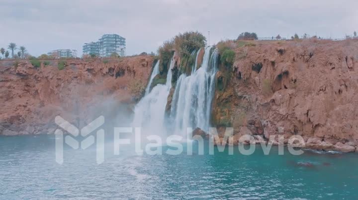 Beautiful stormy waterfall. Dense vegetation on the rock. Blue lagoon and hotel on the rock. Slow motion drone video