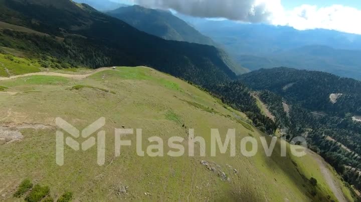 Aerial POV footage of flight over green field and hills. Forests, mountains and green hillsides. View of nature. FPV