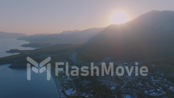Sunset against the backdrop of a mountain landscape. Tourist town by the sea. Aerial drone video footage of a seascape