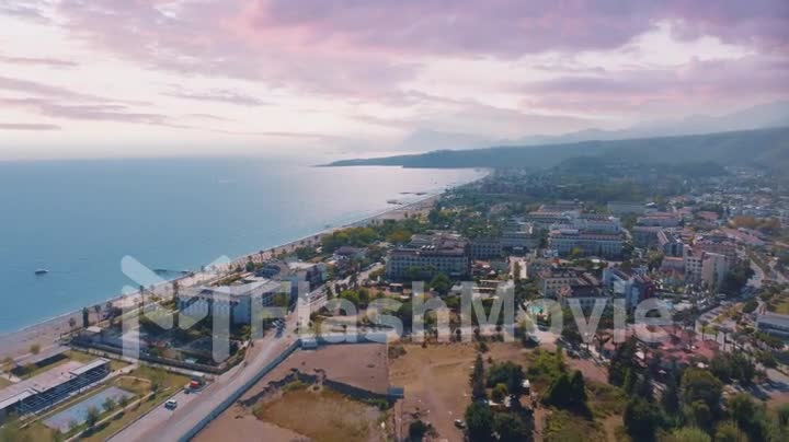 Sunset flight over hotels and coastline. Beautiful purple pink clouds. Mountains in the background. Hotels by the sea