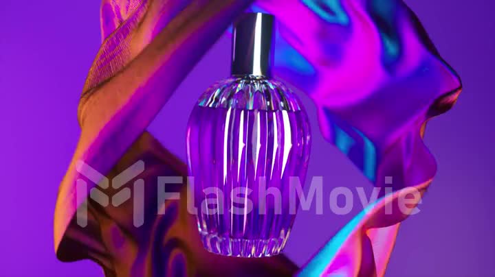 Cosmetic bottle of perfume on a purple background. Fragrant cosmetic product. Silk fabric all around. Flower essence.