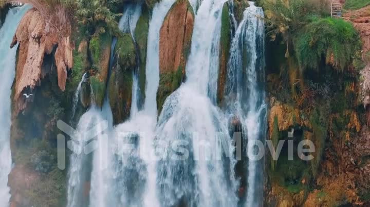 A bird flies in front of a stormy waterfall on a red rock. The element of water. Wildlife concept. Aerial drone footage