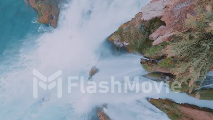 A stormy waterfall falls down from a cliff. Top view. Blue water. Foam. Rock. Wildlife. Aerial drone video footage.