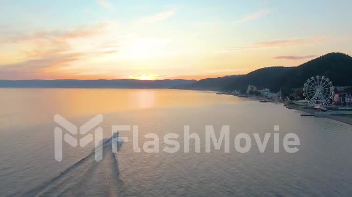 Motor boat at sunset floats on Lake Baikal. Seafaring. Water surface. Top view. Follow the boat. Aerial drone footage