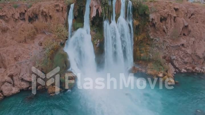 Aerial drone video footage of a waterfall falling off a cliff into a turquoise lagoon. Landscape. Hotels on the coast