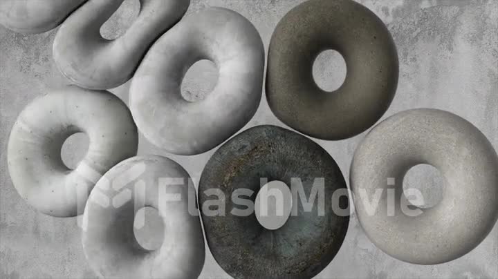 Soft pillows in the form of rings collide with each other against the background of a concrete wall. Dark light grey.