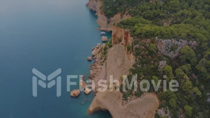 Top view of a rocky shore covered with green trees. Cave in the rock. Blue clear water. Seascape. Drone video footage