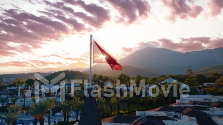 Turkish flag flutters at sunset. Beautiful clouds. Dramatic sky. The territory of the hotel. Mountain landscape.
