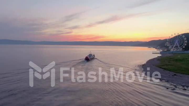 Aerial footage of a white excursion boat on the water of Lake Baikal. Seafaring. Sunset. Top view. Ferris wheel.