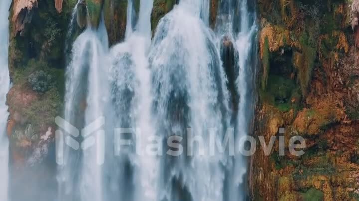 Drone video footage of a natural waterfall close-up. Spray. Green vegetation on the rocks. A bird flies past a waterfall