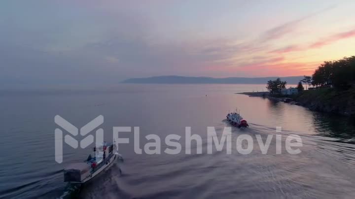Aerial footage of a white excursion boat on the water of lake. Seafaring. Sunset. Top view. People on board.