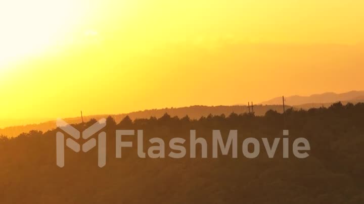 Drone video footage of yellow sunset over mountain hills. Forest on the slope of the mountain. Human and nature