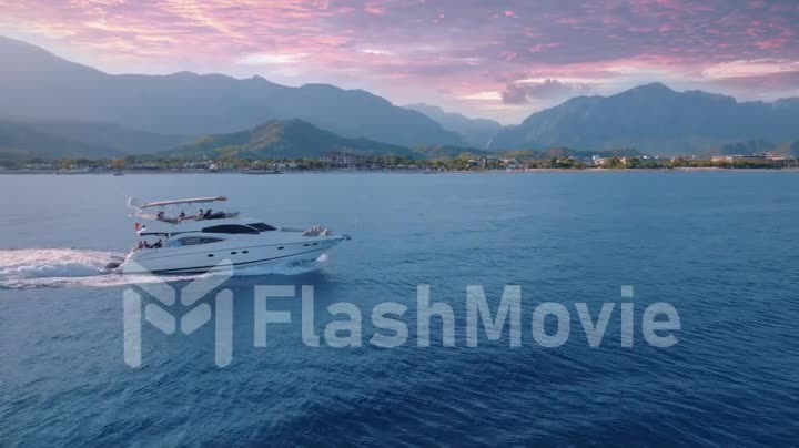 Tourist yacht is sailing fast on the calm blue sea. Sunset. Seascape. Mountains in the background. Aerial drone footage