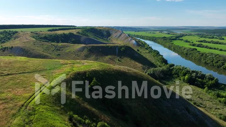 Drone view of green hills, rivers and fields in sunny weather. Beautiful green landscape in the hills. Aerial footage.
