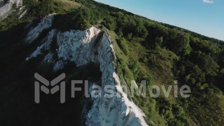 Aerial POV footage of a flight over a white mountain range. Chalk mountain. Green hills, forests and fields. FPV drone.