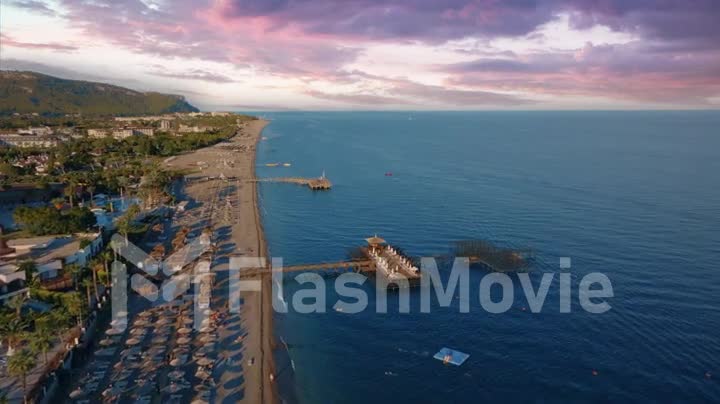 Seascape. Sunset flight over hotels and coastline. Beautiful purple pink clouds. Mountains in the background.