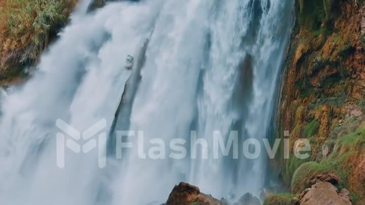 Nature concept. White foamy waterfall flows from the cliff. Close-up drone footage. The power of the elements.