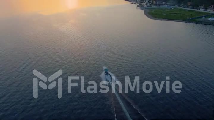 Motor boat at sunset floats on lake. Seafaring. Water surface. Top view. Follow the boat. Aerial drone footage