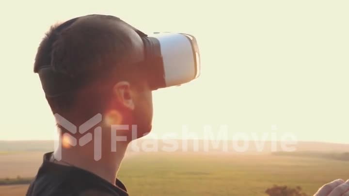 Young man uses virtual reality glasses in nature in a beautiful sunset
