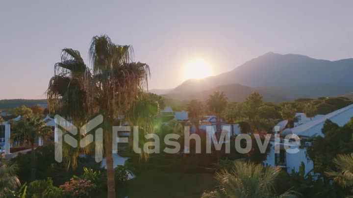Aerial drone video footage. View of the hotel at sunset. Palms. Mountain landscape on the background.