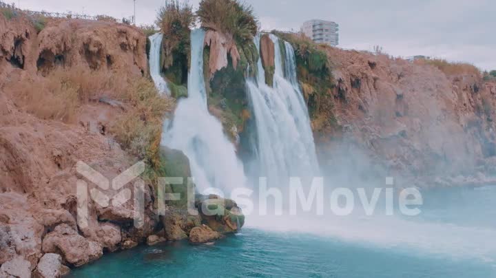 Stormy waterfall on a rock in a tourist place. Hotel on the coast. Harmony with nature. Drone slow motion footage.