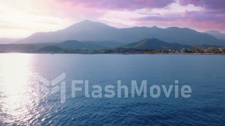 Drone video footage flight over the blue sea at sunset. Beautiful clouds. Mountains in the background. Seascape.