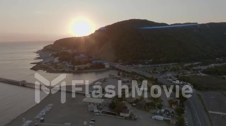 Flight over the coastline at sunset. Drone video footage. Houses, roads, green hills. Human and nature. Top view