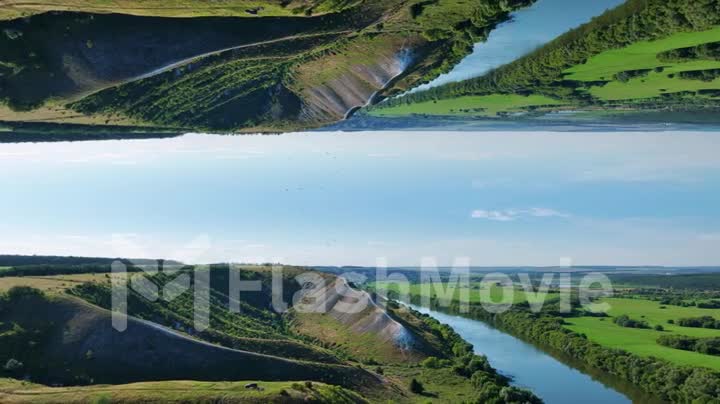 Flight over green hills, field and river on a summer day. Blue sky. Vertical reflection. Drone video 4k footage